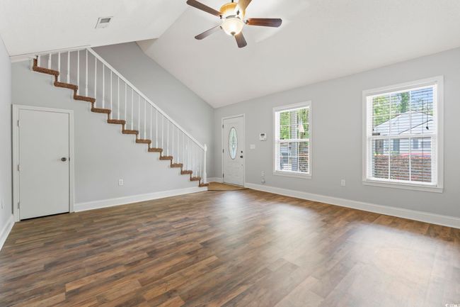Unfurnished living room with stairway, ceiling fan, dark wood-type flooring, and high vaulted ceiling | Image 4