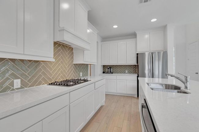 Kitchen with light wood-style flooring, white cabinetry, recessed lighting, stainless steel appliances, and backsplash | Image 10