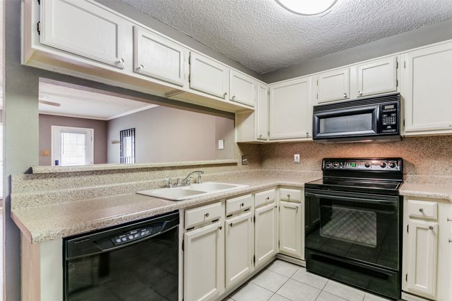 Kitchen featuring black appliances, light tile patterned flooring, light countertops, decorative backsplash, and ornamental molding | Image 12