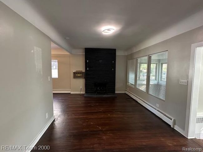 Unfurnished living room with baseboard heating, dark wood finished floors, a large fireplace, and radiator | Image 9
