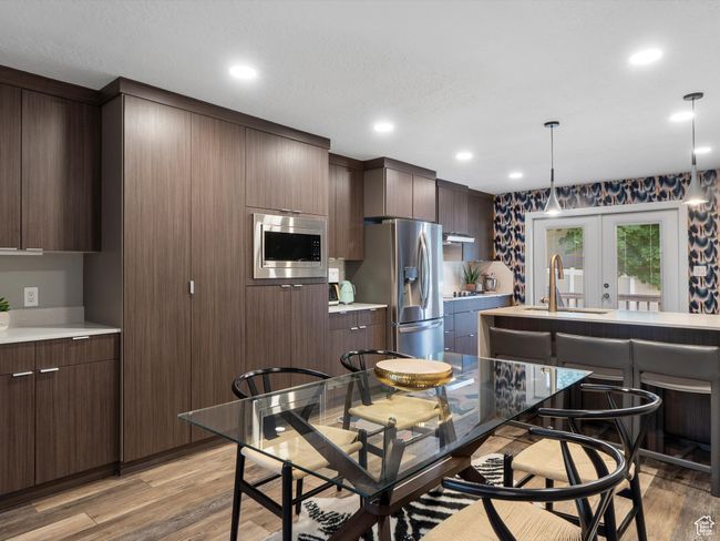 Kitchen featuring appliances with stainless steel finishes, light wood finished floors, hanging light fixtures, light countertops, and dark brown cabinets | Image 13