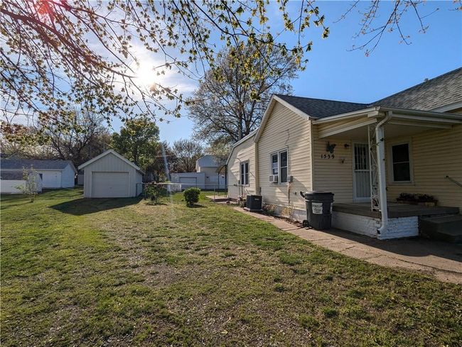 View of property exterior featuring fence, a lawn, roof with shingles, and a detached garage | Image 5