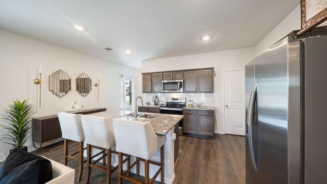 Kitchen with stainless steel appliances, dark brown cabinetry, dark wood-style floors, a center island with sink, and tasteful backsplash | Image 6