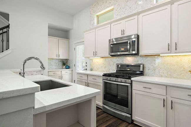 Kitchen with a sink, decorative backsplash, stainless steel appliances, dark wood-type flooring, and white cabinets | Image 13