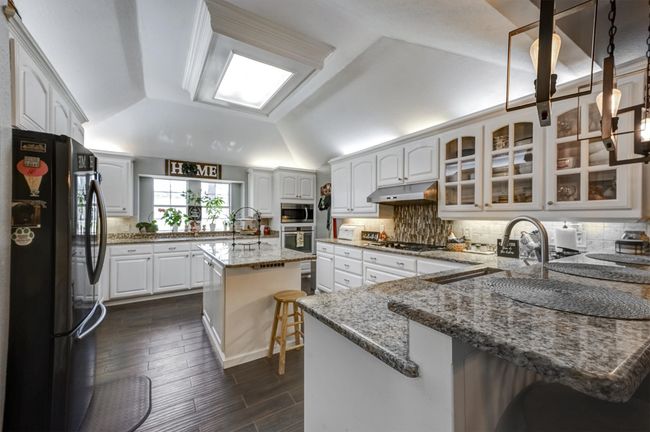 Kitchen featuring a peninsula, under cabinet range hood, a sink, lofted ceiling, and stainless steel appliances | Image 13