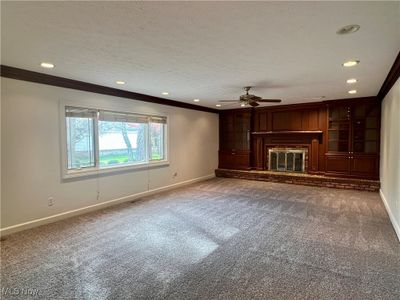 Unfurnished family room with crown molding, carpet, and a brick fireplace | Image 3