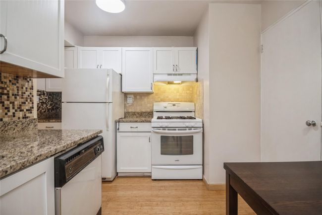 Kitchen with white appliances, under cabinet range hood, white cabinets, and backsplash | Image 8