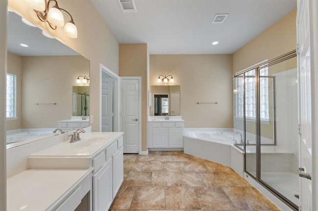 The primary bathroom boasts tile floors, dual vanities with sinks, a relaxing jacuzzi tub, a step-in shower with a bult-in bench, and a spacious walk-in closet, combining luxury and functionality. | Image 34