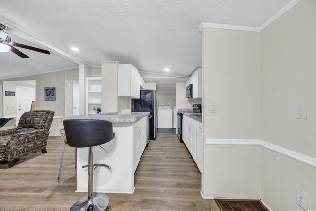 Kitchen featuring appliances with stainless steel finishes, a ceiling fan, light wood finished floors, a breakfast bar area, and white cabinets | Image 10