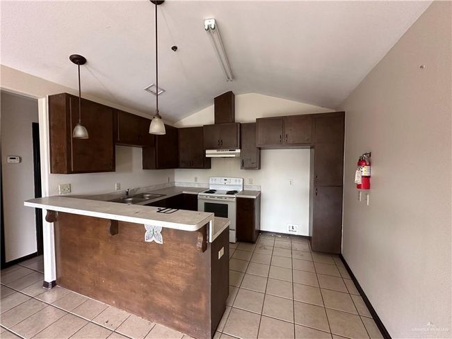 Kitchen featuring light tile patterned flooring, pendant lighting, vaulted ceiling, white electric range oven, and kitchen peninsula | Image 6