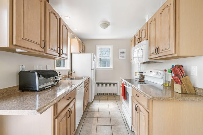 Kitchen featuring light brown cabinets, a sink, white appliances, light tile patterned floors, and radiator | Image 14