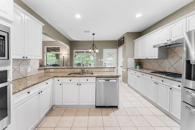 Kitchen featuring stainless steel appliances, under cabinet range hood, a sink, backsplash, and a chandelier | Image 10