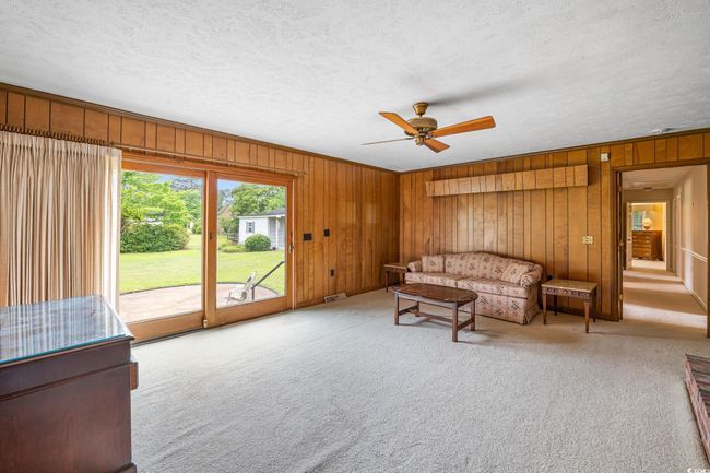 Living area with a ceiling fan, carpet floors, wooden walls, and a textured ceiling | Image 14