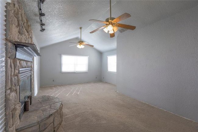 Unfurnished living room with a textured ceiling, ceiling fan, a stone fireplace, lofted ceiling, and carpet floors | Image 19