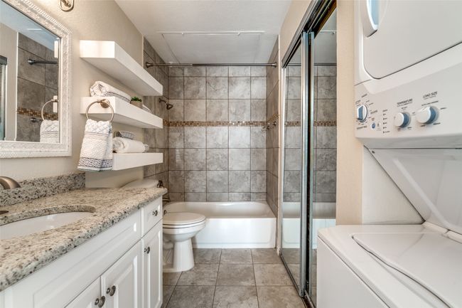 Bathroom featuring tub / shower combination, stacked washer and clothes dryer, toilet, vanity, and tile patterned flooring | Image 14