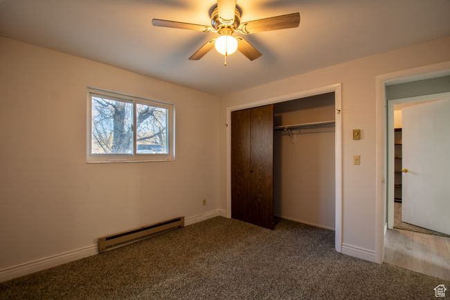 Unfurnished basement bedroom with carpet flooring, a closet, ceiling fan, and a baseboard heating unit | Image 10