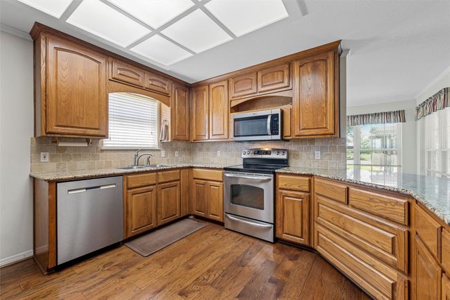 Kitchen with dark wood-style flooring, crown molding, stainless steel appliances, and a sink | Image 11