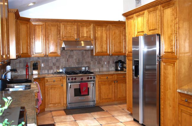 Kitchen featuring under cabinet range hood, stainless steel appliances, and brown cabinets | Image 12