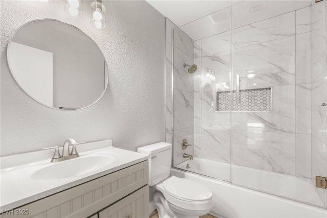 Bathroom with a textured wall, bath / shower combo with glass door, toilet, and vanity | Image 21