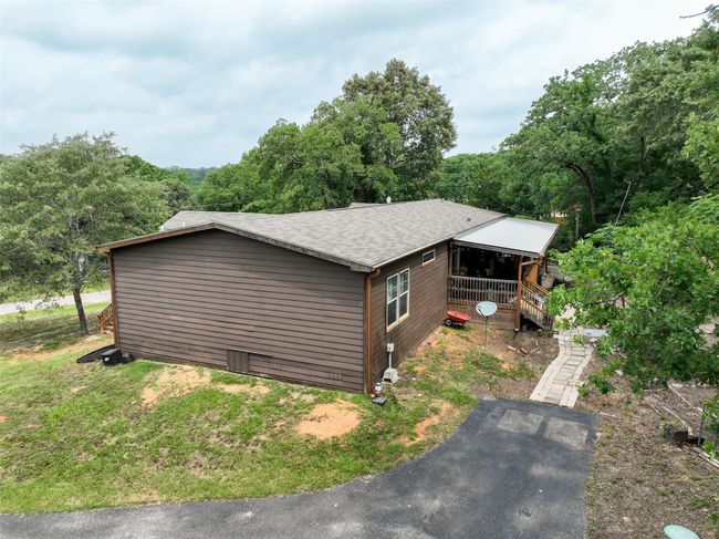 View of property exterior featuring a shingled roof and a view of trees | Image 5
