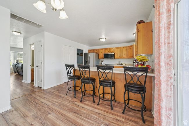 Kitchen featuring appliances with stainless steel finishes, a peninsula, light wood-style flooring, a breakfast bar area, and light countertops | Image 7