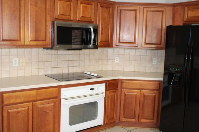 Kitchen with brown cabinetry, light countertops, and black appliances | Image 17