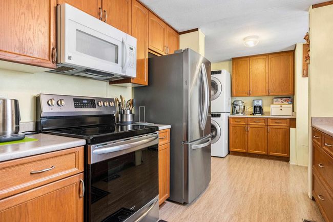 Kitchen featuring light wood-style flooring, stacked washer / drying machine, white microwave, brown cabinetry, and stainless steel electric stove | Image 13