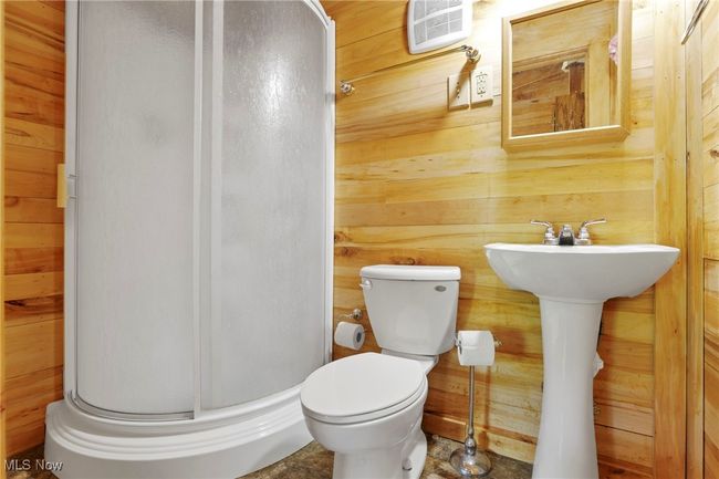 Bathroom with a stall shower, wood walls, toilet, and a sink | Image 25