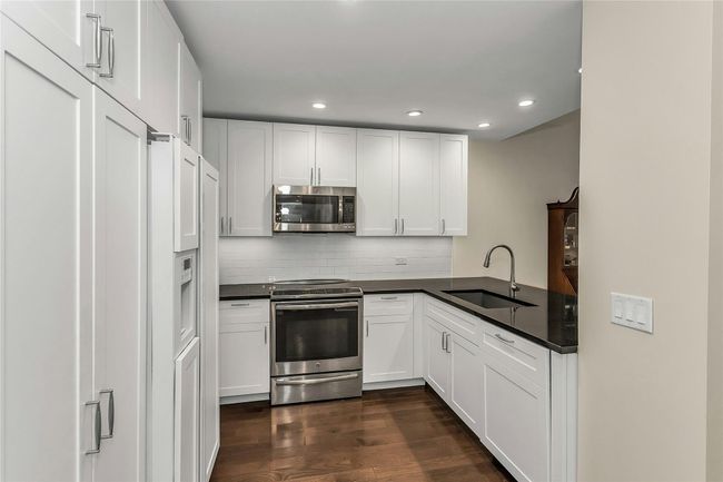 Kitchen featuring appliances with stainless steel finishes, a sink, dark wood finished floors, dark countertops, and decorative backsplash | Image 8