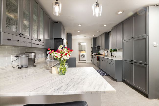 Kitchen with tasteful backsplash, washer / clothes dryer, glass insert cabinets, light stone countertops, and gray cabinets | Image 11