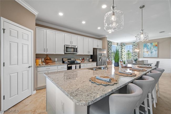 Kitchen featuring white cabinets, a sink, appliances with stainless steel finishes, crown molding, and a spacious island | Image 16