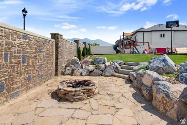 View of patio with an outdoor fire pit, a mountain view, a playground, and a fenced backyard | Image 24