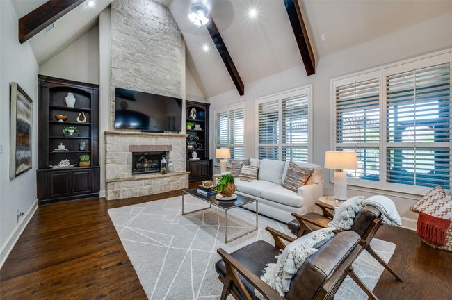 This impressive living space features soaring two-story ceilings, luxurious wood beams, and a floor-to-ceiling stone fireplace that serves as the stunning centerpiece of the room. | Image 15