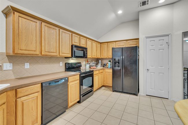 Kitchen featuring black appliances, vaulted ceiling, light tile patterned flooring, light countertops, and decorative backsplash | Image 15