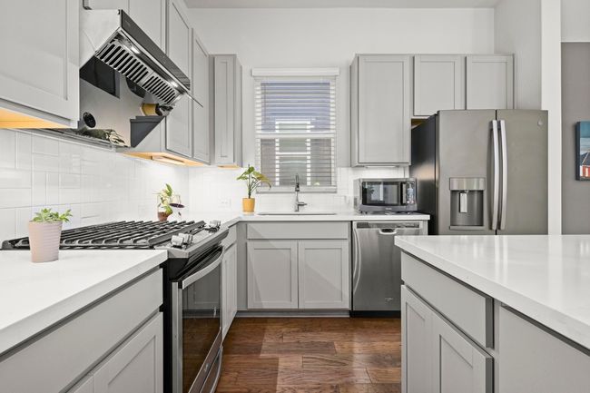 Kitchen featuring stainless steel appliances, extractor fan, tasteful backsplash, light countertops, and dark wood-style floors | Image 13