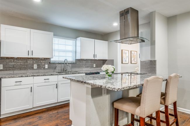 Kitchen featuring island range hood, dark wood-type flooring, light stone counters, a kitchen bar, and decorative backsplash | Image 18
