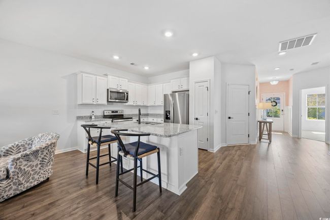 Kitchen with white cabinetry, dark wood-type flooring, visible vents, a kitchen island with sink, and appliances with stainless steel finishes | Image 5