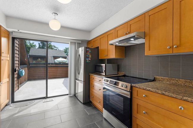 Kitchen with appliances with stainless steel finishes, under cabinet range hood, brown cabinetry, a textured ceiling, and dark tile patterned flooring | Image 16