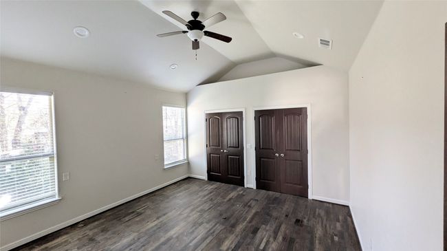 Unfurnished bedroom with multiple closets, lofted ceiling, visible vents, dark wood-type flooring, and baseboards | Image 6