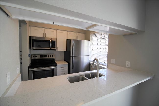 Kitchen with appliances with stainless steel finishes, light stone counters, white cabinets, and a peninsula | Image 5