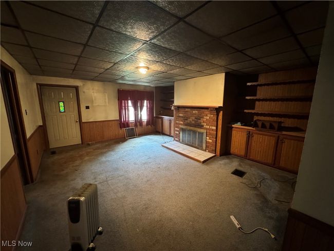 Unfurnished living room featuring visible vents, a fireplace, radiator, a paneled ceiling, and wainscoting | Image 6