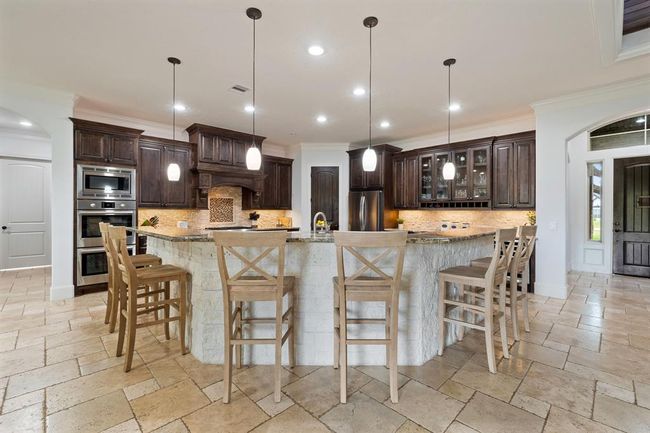 An abundance of additional seating can be found at this bar-height, wrap-around, countertop. The clean white stone façade mimics the backsplash just beyond. Pull up a chair and await the delicious feast the home chef is preparing. | Image 16