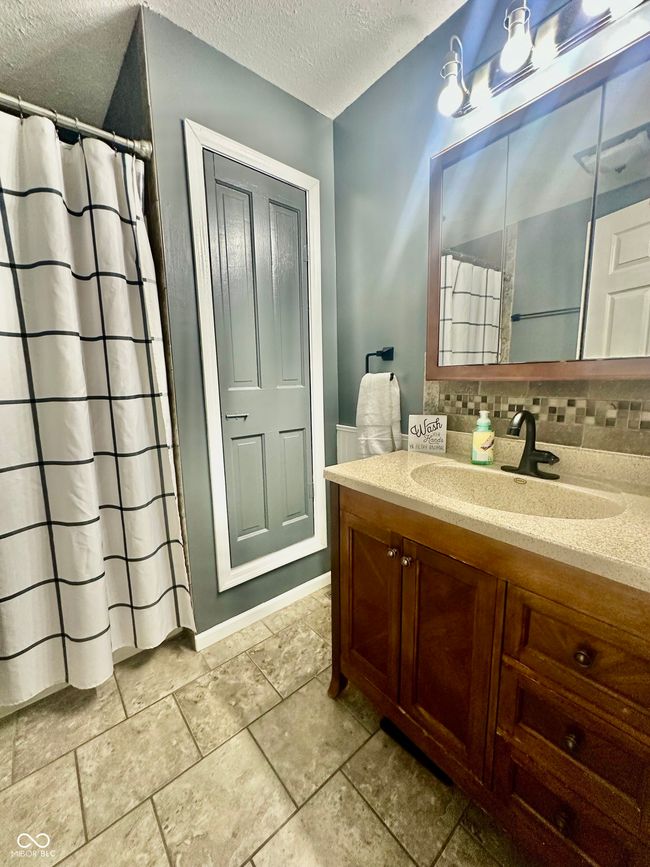 bathroom featuring a textured ceiling, vanity, decorative backsplash, and curtained shower | Image 25