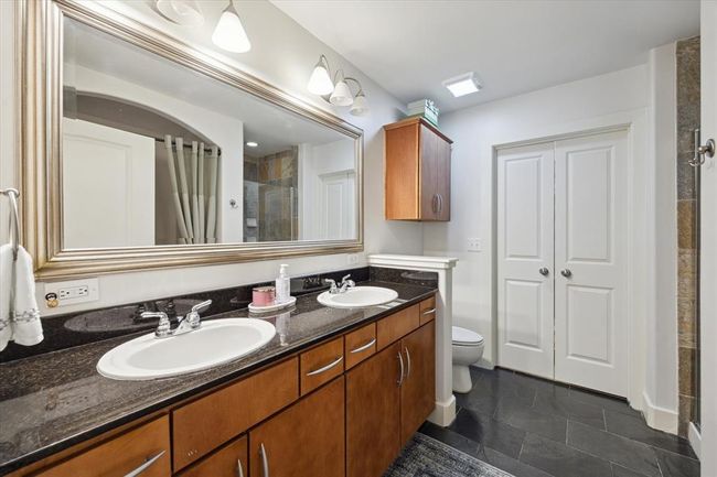 The primary bath features dual sinks, a large wall mirror, overhead cabinetry, and chic slate flooring. Double doors open to the spacious walk-in closet. | Image 10