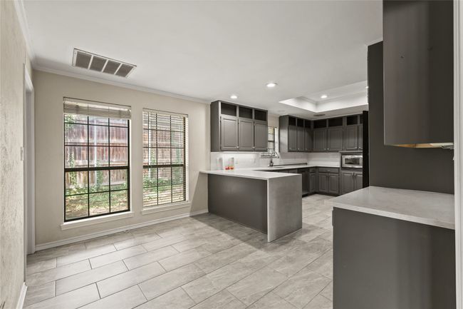 Kitchen with gray cabinetry, stainless steel microwave, ornamental molding, a peninsula, and light countertops | Image 16