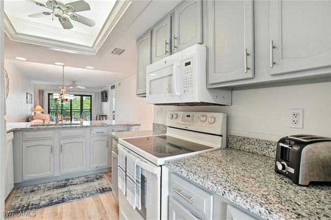 Kitchen with white appliances, a raised ceiling, a ceiling fan, light wood-style floors, and recessed lighting | Image 16