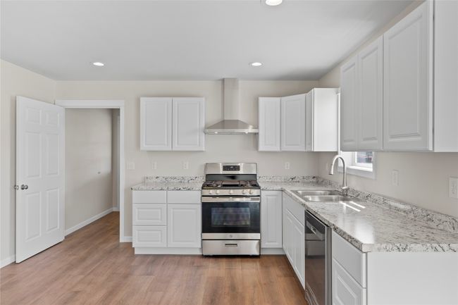 Kitchen with appliances with stainless steel finishes, white cabinetry, a sink, light wood-type flooring, and wall chimney range hood | Image 35