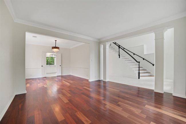 Unfurnished living room featuring wood finished floors, ornate columns, stairway, crown molding, and a chandelier | Image 11