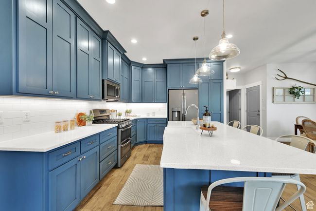 Kitchen featuring stainless steel appliances, a kitchen bar, blue cabinets, light wood-style floors, and recessed lighting | Image 10