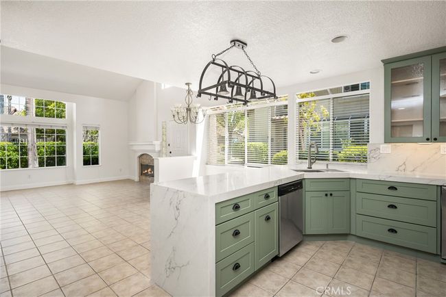 The open-concept kitchen features stainless steel appliances, a wine fridge, and flows seamlessly into the living area with a cozy fireplace and access to a private patio. | Image 16